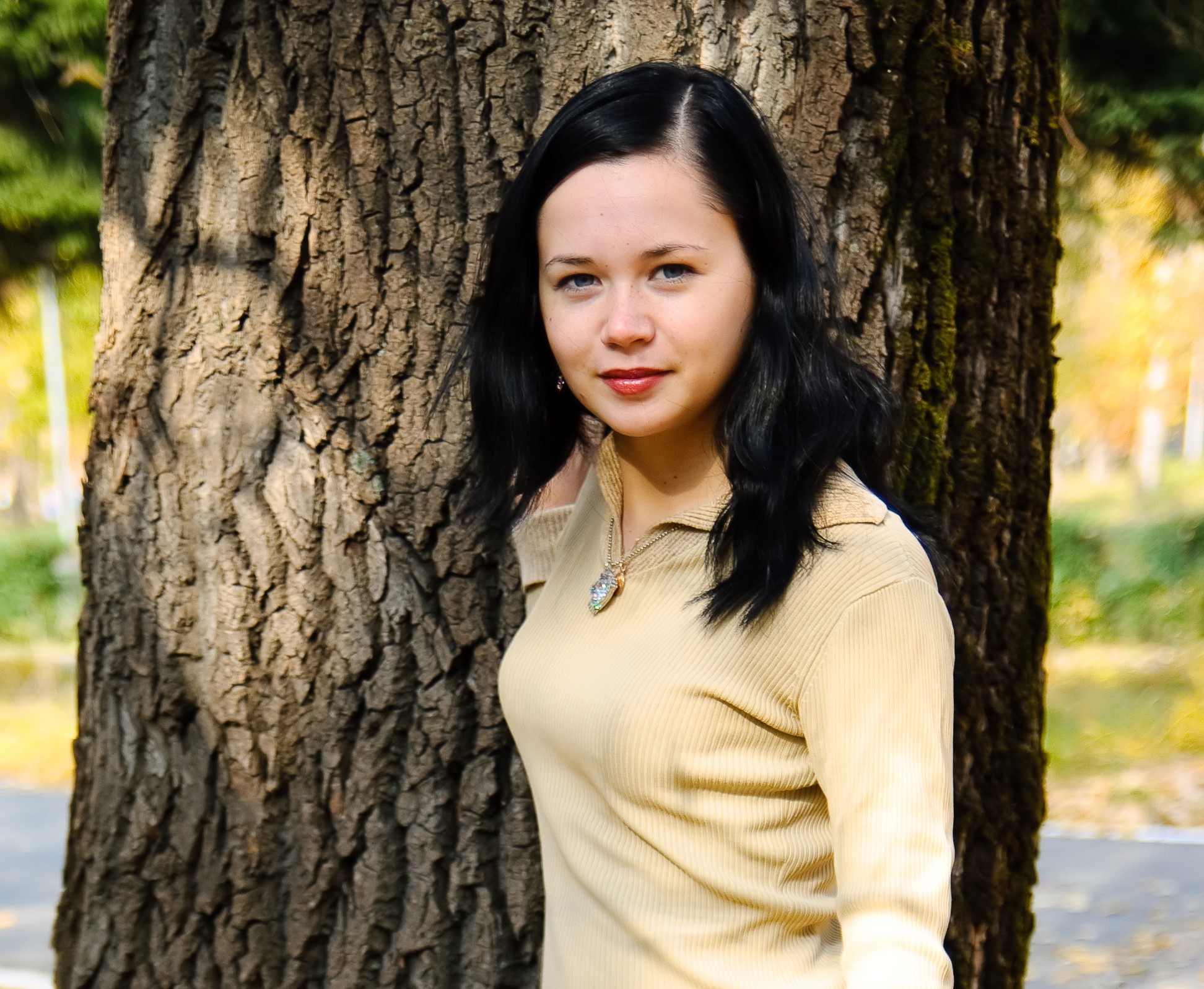 woman staring at camera, standing in front of a tree.